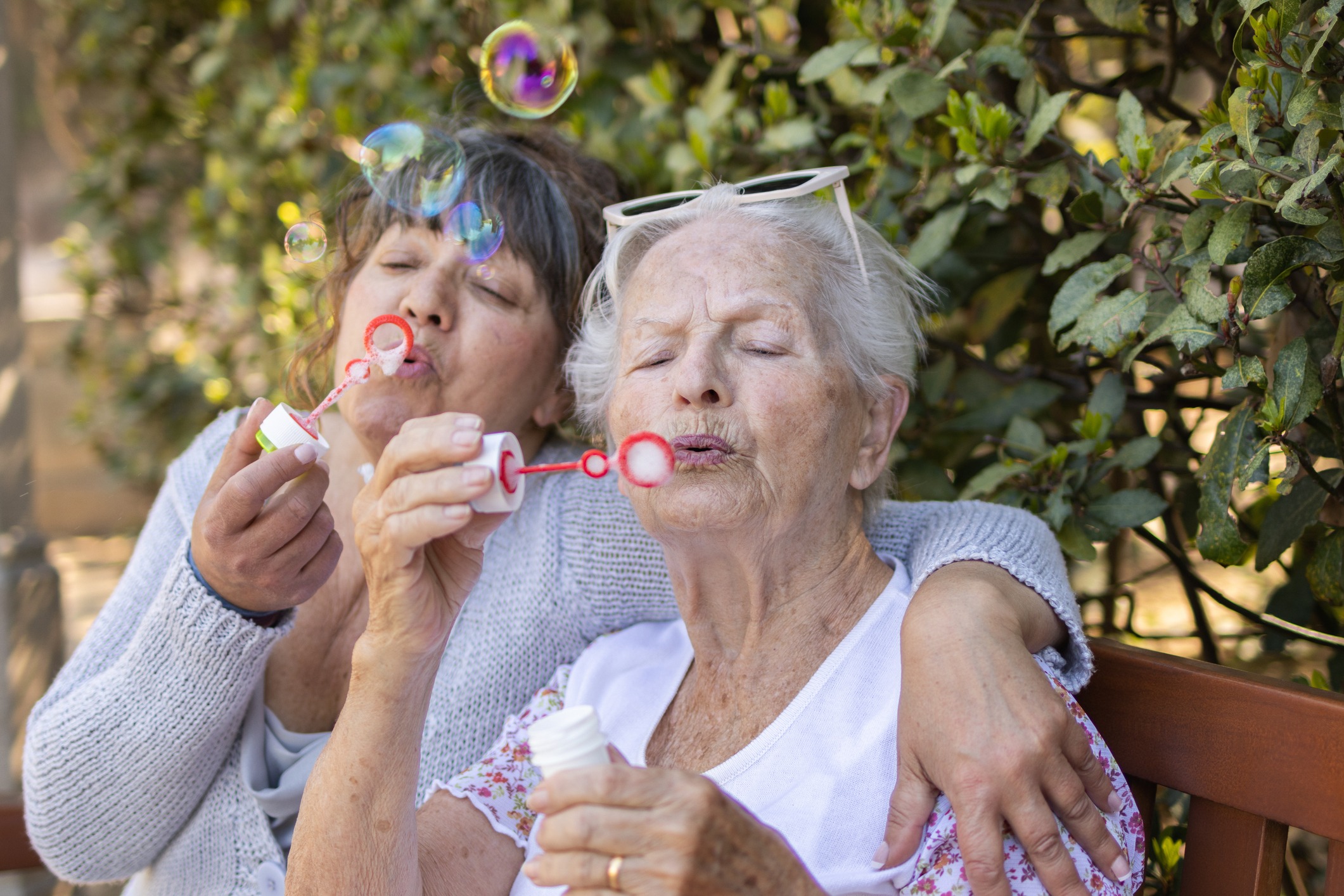 elderly mother and her senior daughter blowing soap bubbles for summer fun. two generations of women in the family.